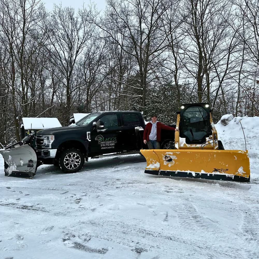 Snow removal equipment and truck in winter landscape with operator in snowy setting.